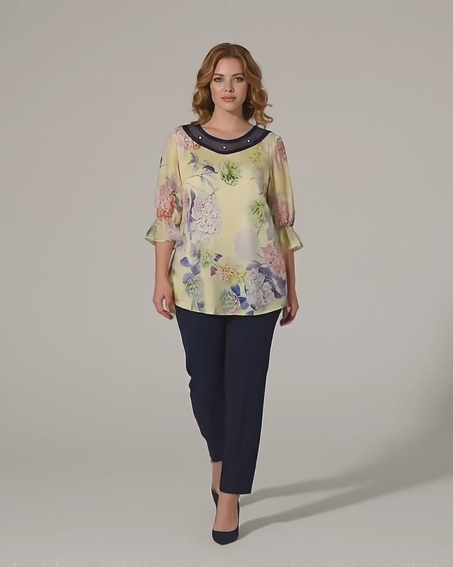 Макси модел върви бавно към камерата в студио на неутрален фон, облечена с Официална разкроена макси туника на цветя в жълто с перли и тюл