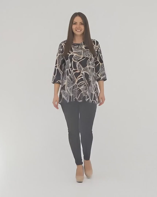 Студийно видео на макси модел на неутрален фон, който върви бавно към камерата и носи Разкроена туника с абстрактен принт и декоративна панделка