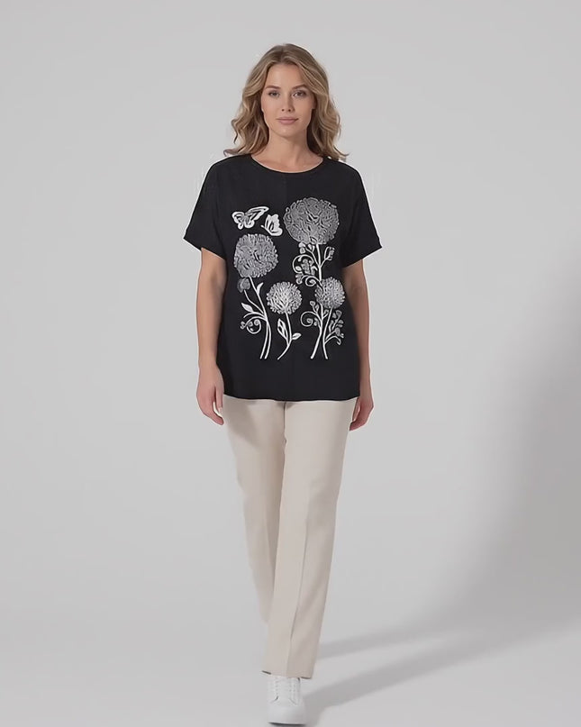 Видео представяне в студийна среда с неутрален фон, показващо как макси модел върви бавно към камерата, облечена в Черна лятна макси туника с ефектна апликация на цветя