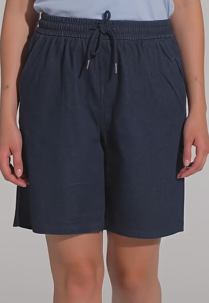 Студийно видео с неутрален фон, показващо макси модел, която върви бавно към камерата, облечена в Къси тъмносини шорти с джобове и ластик в големи размери