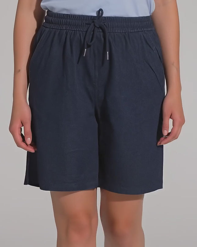 Студийно видео с неутрален фон, показващо макси модел, която върви бавно към камерата, облечена в Къси тъмносини шорти с джобове и ластик в големи размери