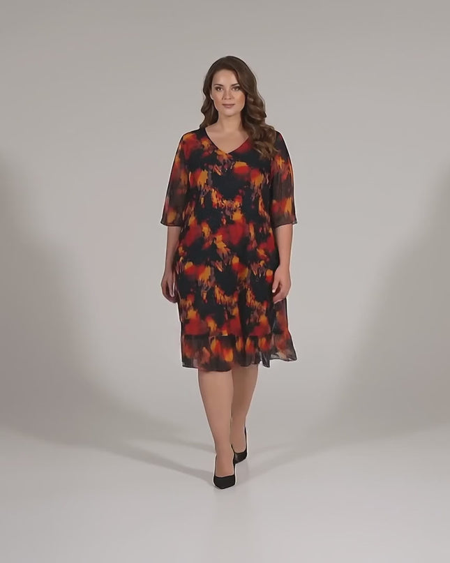 Видео в студийна среда, в което плюс сайз модел върви бавно към камерата, облечена с Официална черна макси рокля с шифон и огнен принт големи размери