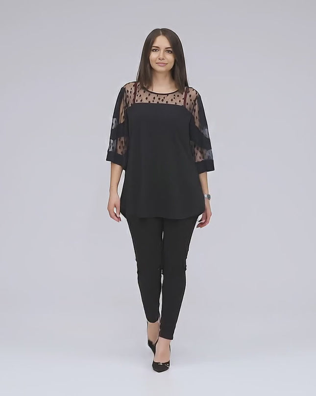 Макси модел, облечена в Черна официална туника с тюл на точки и 3/4 ръкави, върви бавно към камерата в студийна среда на неутрален фон