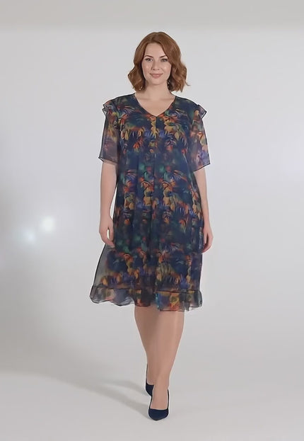 В студийна среда плюс сайз модел върви бавно към камерата, носейки Официална макси рокля от цветен шифон с ефектен ръкав