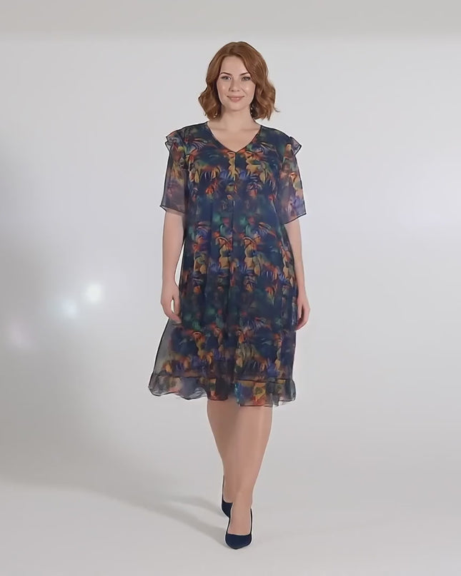 В студийна среда плюс сайз модел върви бавно към камерата, носейки Официална макси рокля от цветен шифон с ефектен ръкав