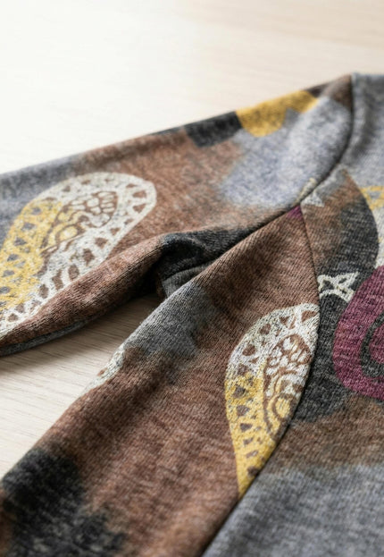 Детайл отблизо на материята и ръкава на разкроена ежедневна рокля с пейсли мотиви в кафяво, заснета върху дървен фон.
