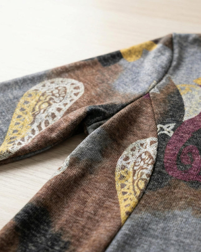 Детайл отблизо на материята и ръкава на разкроена ежедневна рокля с пейсли мотиви в кафяво, заснета върху дървен фон.