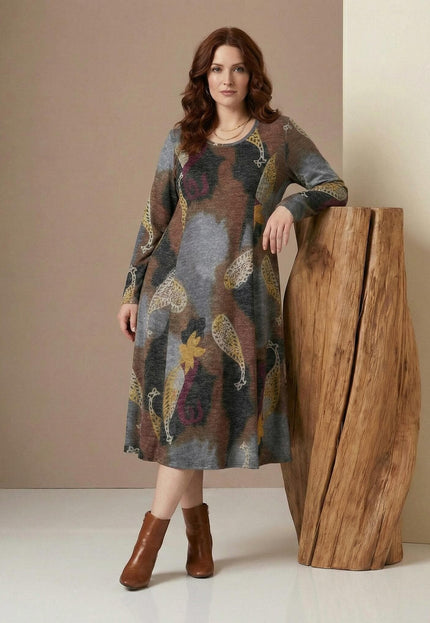 Разкроена ежедневна рокля с пейсли мотиви в кафяво и сиво, представена в цял ръст върху модел до дървен декор.