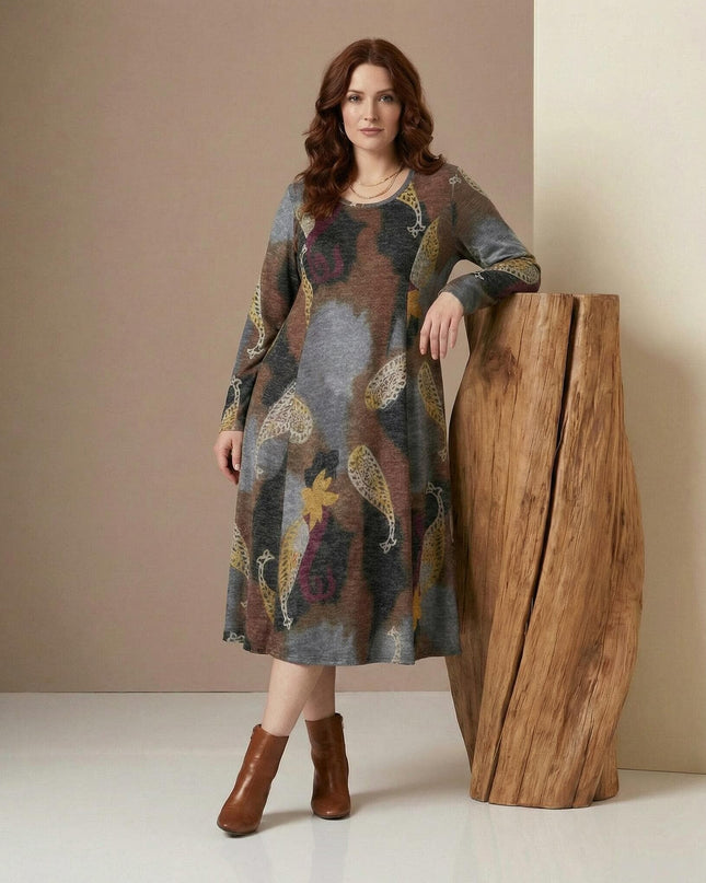 Разкроена ежедневна рокля с пейсли мотиви в кафяво и сиво, представена в цял ръст върху модел до дървен декор.