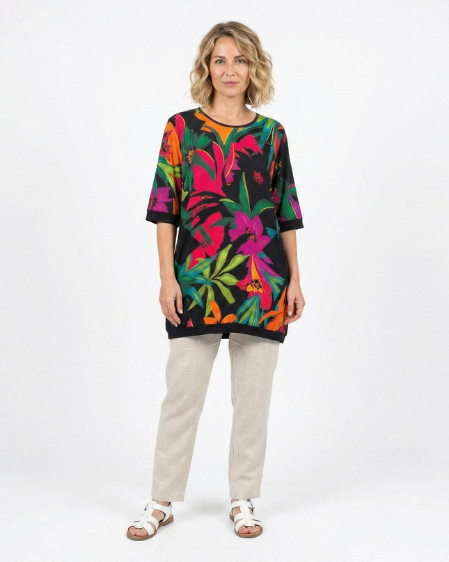 Дама в цял ръст, облечена в шарена лятна туника големи размери с ярък тропически флорален принт и къси ръкави.