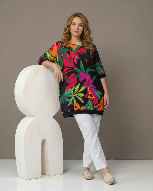 Шарена лятна туника големи размери с тропически флорален принт, представена в цял ръст от модел в комбинация с бели панталони.
