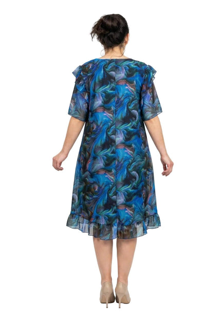 Шарена официална рокля големи размери в сини нюанси, заснета отзад. Вижда се свободният гръб на модела, ефирните шифонени ръкави и воланът в долната част.