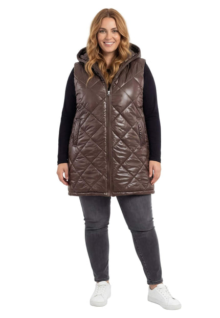 Шоколадово кафяв дълъг ватиран елек с качулка и лек гланц, представен върху модел в цял ръст. Виждат се диагоналното капитониране и удобните странични джобове.