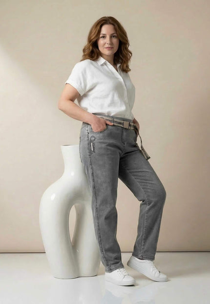 Дамски сиви макси дънки с права кройка и текстилен колан. Представени в цял ръст от модел с бяла риза, облегнат на декоративна фигура.