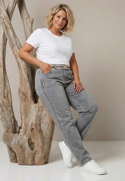 Сиви ежедневни макси дънки с права кройка и текстилен колан. Кадър в цял ръст на модел, представящ визията, облегнат на масивно дърво.