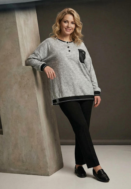 Светлосива туника меланж с декоративен джоб и мрежа, заснета в цял ръст върху модел. Виждат се черните кантове на подгъва и ръкавите, както и копчетата на деколтето.