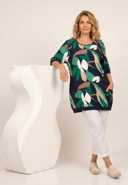 Тъмносиня лятна туника големи размери с флорален принт. Модел в цял ръст, демонстриращ разкроената кройка, обло деколте и предни джобчета, на бял фон.