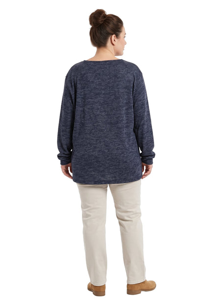 Жена в гръб с тъмносиня туника с дълги ръкави и светли панталони на бял фон.