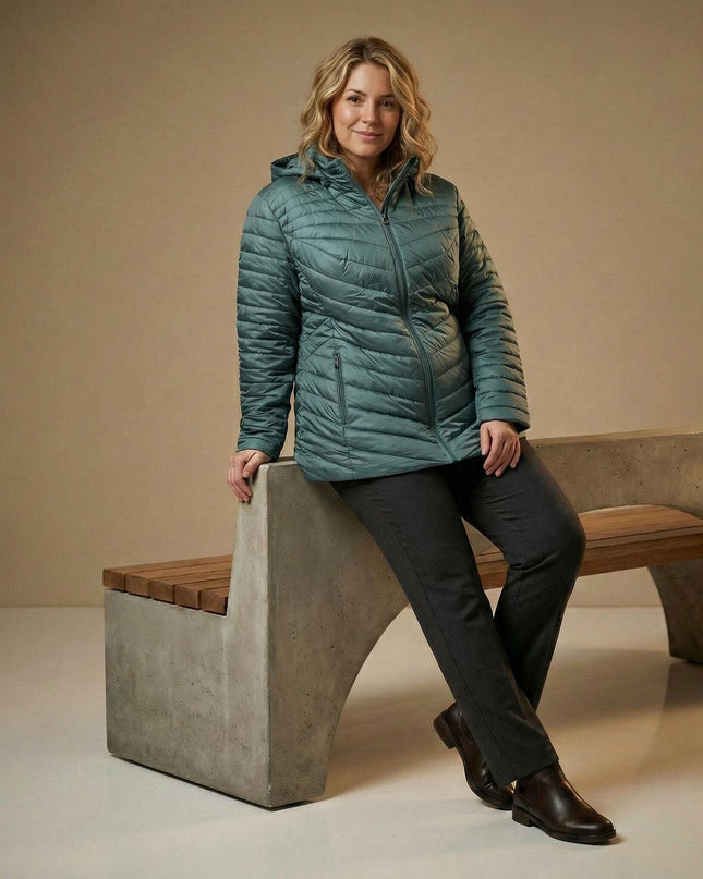 Зелено дамско макси яке с качулка и V-образно капитониране, представено върху модел в седнала позиция на пейка.